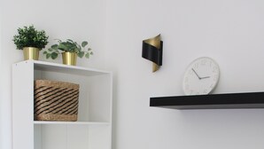 Ein Wohnzimmer mit grauem Sofa, einem weißen Regal mit Körben, einer Uhr und zwei Zimmerpflanzen.