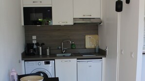 A compact kitchen with a washing machine, dishwasher, and a small dining table with a chair. - Studio 433 Les Chênes verts (Mollans-sur-Ouvèze)