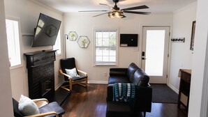 A living room with a fireplace, a black leather sofa, a wooden rocking chair, a black leather couch, and a ceiling fan.