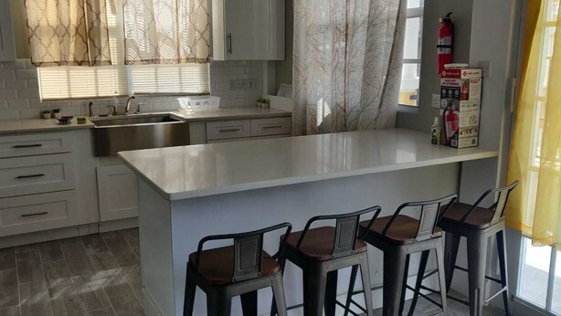 A modern kitchen with white cabinets, a marble countertop, and a bar area with stools.