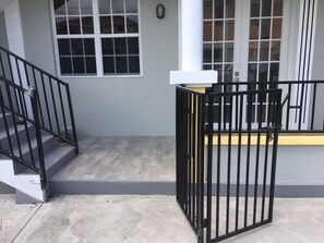 A residential building with a grey exterior, a black metal gate, and a staircase leading to a landing.