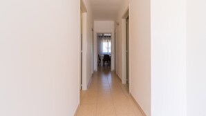 A narrow hallway with a tiled floor leading to a dining area with a table and chairs.
