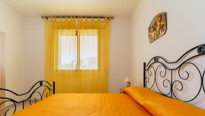 A bedroom with a bed, curtains, a nightstand, and a wall-mounted lamp.