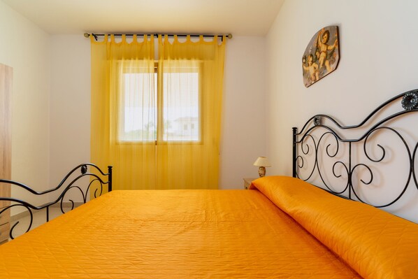 Un dormitorio con cama, cortinas, mesita de noche y una lámpara de pared.
