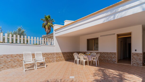 A covered patio with a stone floor, white chairs, and a table.