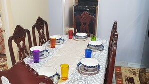 A dining table set with plates, bowls, and colorful glasses, surrounded by wooden chairs. - Mckay's Home Away from Home (Hatfield)