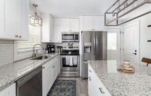 Una cocina moderna con armarios blancos, electrodomésticos de acero inoxidable, encimeras de granito y una alfombra estampada.