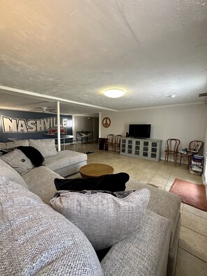 Un salón con un sofá modular, una mesa de centro y un televisor. Se ve una pared con un símbolo de paz y un letrero que dice 'Nashville Museum'.