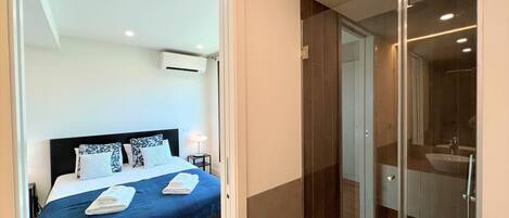 Habitació d'hotel moderna amb un llit gran, un espai de bany amb dutxa de vidre i bany visible.