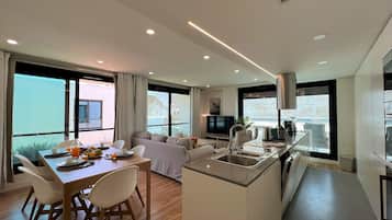 Una cocina moderna con una isla central, una zona de comedor con mesa y sillas, y una sala de estar con sofá.