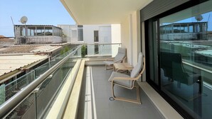 A balcony with glass railings, two lounge chairs, and a view of the cityscape. - FARO DESIGN 1 by HOMING (Faro)