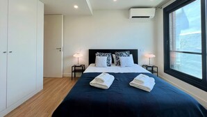 A modern hotel room with a large bed, two bedside tables with lamps, a wardrobe, an air conditioning unit, and a window with a view. - FARO DESIGN 1 by HOMING (Faro)
