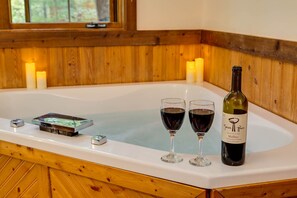 A wooden cabin interior with a white bathtub, two wine glasses, and a bottle of wine.