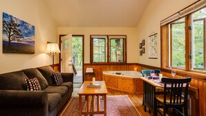 Ein gemütliches Wohnzimmer mit Sofa, Couchtisch und Essbereich mit Tisch und Stühlen. In der Ecke steht eine Badewanne und eine Tür führt in einen Garten.