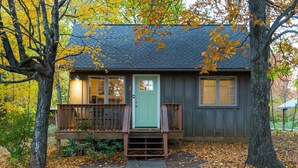 Eine Holzhütte mit Veranda, einer grünen Tür und einem Fenster mit Blick auf die umliegenden Bäume.