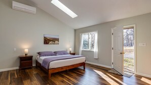 Un dormitorio con cama, mesita de noche, aire acondicionado de pared, tragaluz, ventana y puerta.