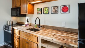 Una cocina con armarios de madera, un lavamanos de acero inoxidable, un microondas, una estufa y un refrigerador. Hay cuatro cuadros en la pared.