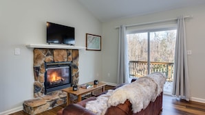 Una sala de estar acogedora con chimenea de piedra, un televisor de pantalla plana, una mesa de centro de madera y un sofá de cuero.