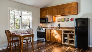 Una cocina con armarios de madera, un refrigerador negro, un microondas y una mesa de comedor con sillas.