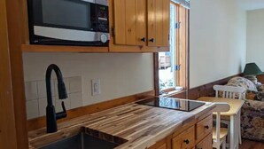 A kitchen with wooden cabinets, a microwave, a sink, and a dining area with a table and chairs. - Kennedy Ridge Cabin--1BR, jacuzzi, kitchenette (Lyndhurst)