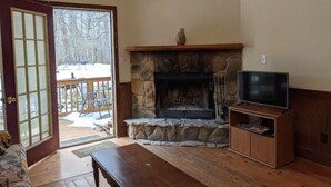A living room with a stone fireplace, a television on a wooden stand, and a sliding glass door leading to an outdoor area. - Kennedy Ridge Cabin--1BR, jacuzzi, kitchenette (Lyndhurst)