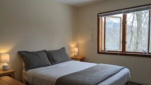 A bedroom with a bed, bedside tables, a window, and a view of trees. - Kennedy Ridge Cabin--1BR, jacuzzi, kitchenette (Lyndhurst)
