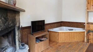 A room with a stone fireplace, a wooden TV stand, a large wooden bathtub, and a wooden shelf. - Kennedy Ridge Cabin--1BR, jacuzzi, kitchenette (Lyndhurst)
