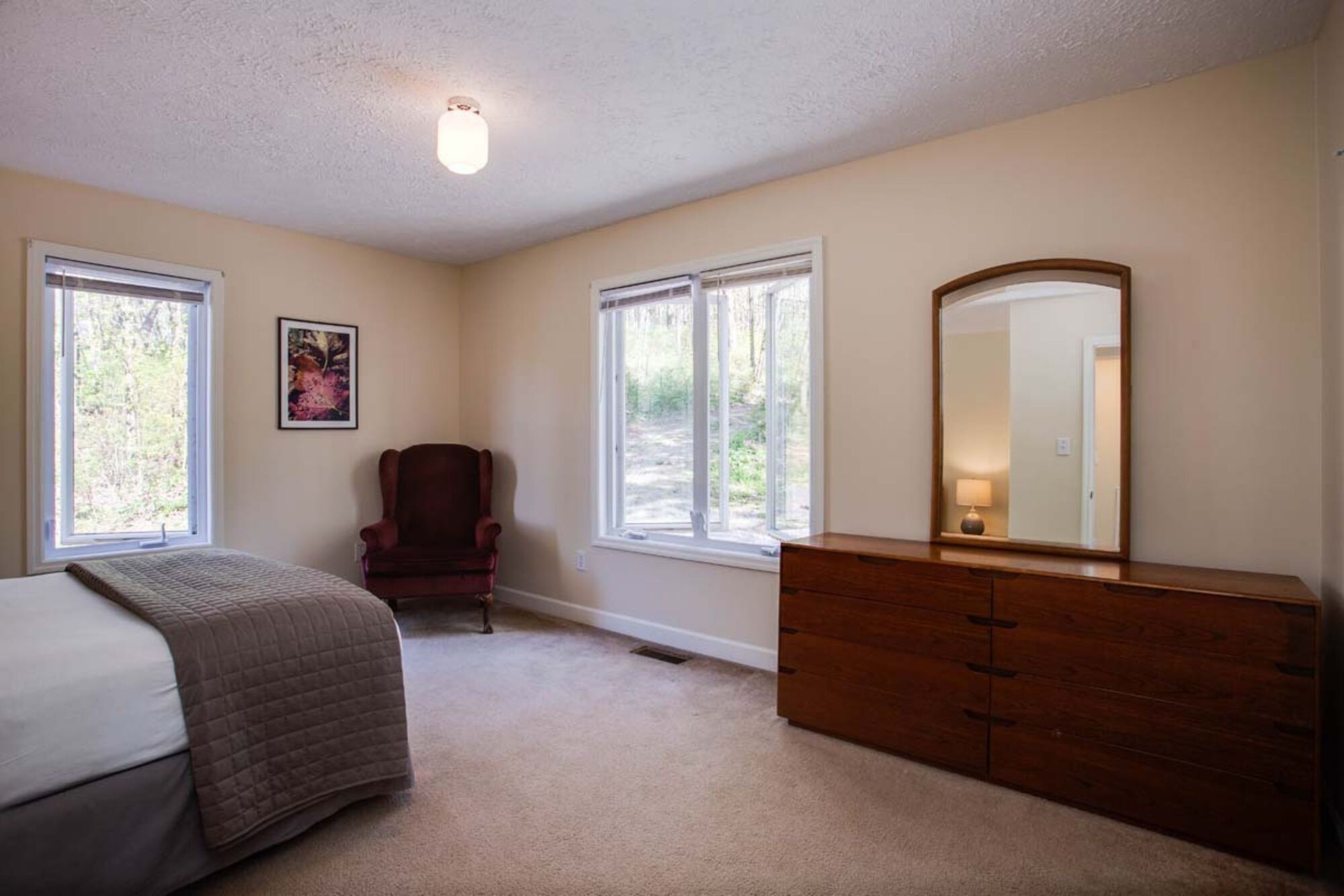 Une chambre à coucher avec un lit, une chaise, une commode et deux fenêtres.