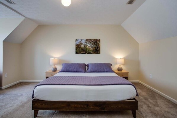 A bedroom with a large bed, two bedside lamps, and a wall-mounted picture.
