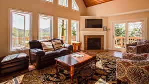 A spacious living room with a fireplace, large windows, and a cozy seating area. - Ravens Roost--mountain views, hot tub, fireplace (Lyndhurst)
