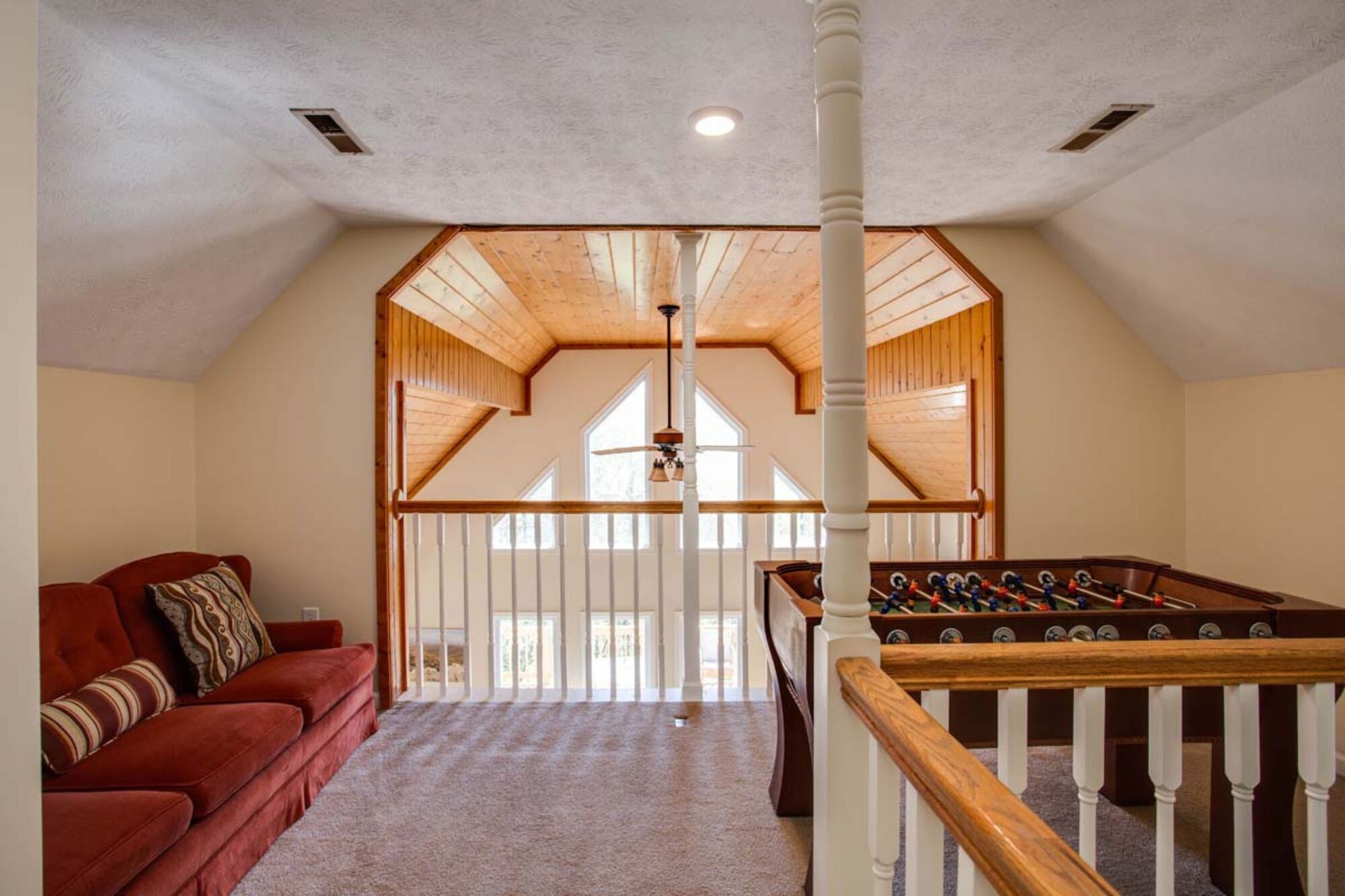 A spacious room with a red sofa, a foosball table, and a high ceiling with wooden beams.