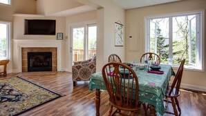 A dining area with a fireplace, wooden chairs, a table with a green tablecloth, and large windows with a view of trees. - Ravens Roost--mountain views, hot tub, fireplace (Lyndhurst)