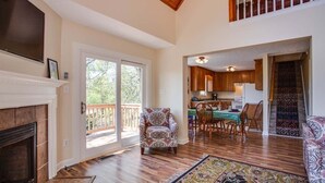 A spacious living room with hardwood floors, a fireplace, a patterned armchair, and a dining area with a table and chairs. - Ravens Roost--mountain views, hot tub, fireplace (Lyndhurst)