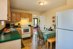 A kitchen with wooden cabinets, a stove, a microwave, and a dining area with a table set for two. - Sherando Cabin--hot tub, kitchen, fireplace (Lyndhurst)