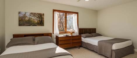 A bedroom with two beds, a nightstand, a window with curtains, a ceiling fan, and a painting on the wall.