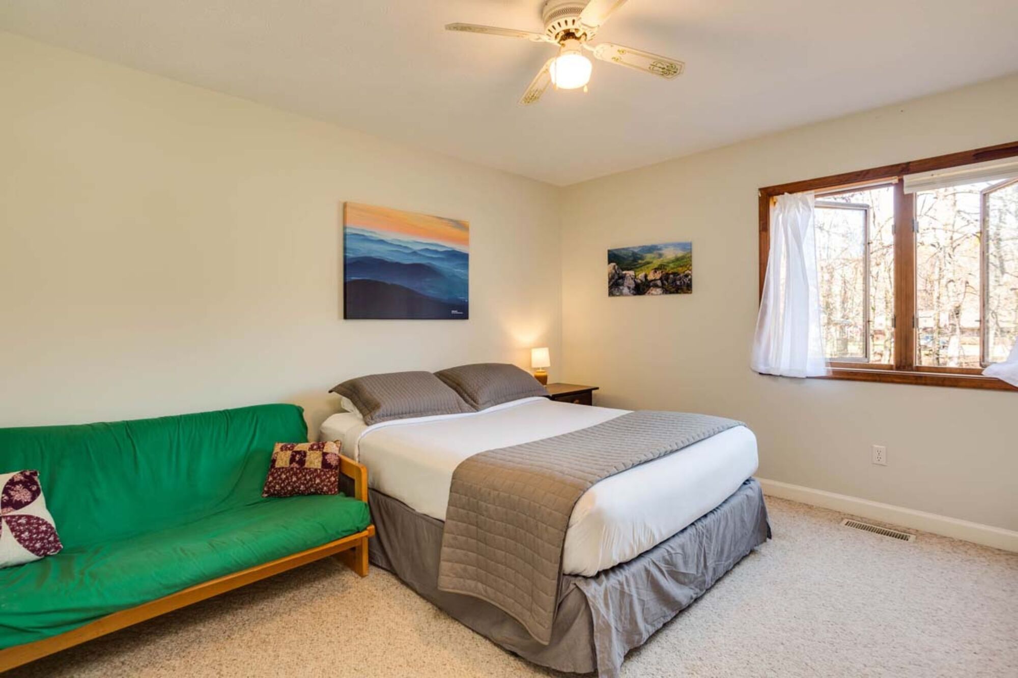 A bedroom with a bed, a green sofa, a ceiling fan, and two wall-mounted paintings.
