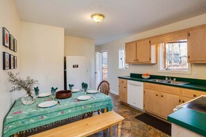 Un coin repas avec une table dressée pour deux personnes, un banc et une vue sur la cuisine, avec ses meubles en bois et une fenêtre.