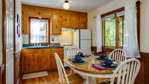 Une cuisine en bois avec une table à manger pour quatre personnes, des placards en bois, un réfrigérateur et une fenêtre avec des rideaux.