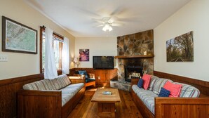 Un salon chaleureux, doté de meubles en bois, d’une cheminée en pierre, d’un ventilateur de plafond et d’un téléviseur à écran plat.