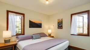 Une chambre à coucher comprenant un lit, deux tables de chevet, deux lampes et deux fenêtres avec des rideaux.