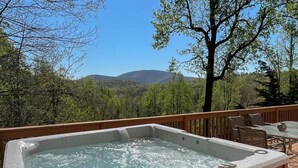 Un bain à remous sur une terrasse en bois, avec vue sur les montagnes et les arbres.