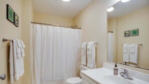 Une salle de bain avec des toilettes blanches, un lavabo avec un miroir et un rideau de douche.
