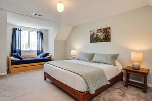 Une chambre avec un grand lit, une fenêtre avec des rideaux, une table de chevet avec une lampe et un tableau accroché au mur.