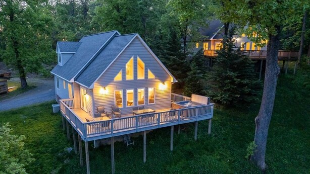 Une maison à deux étages avec une terrasse, entourée d’arbres.