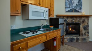 A kitchen with wooden cabinets, a microwave, a stove, a sink, a refrigerator, and a stone fireplace. - White Rock Cabin--1BR, ADA, kitchenette, fireplace (Lyndhurst)