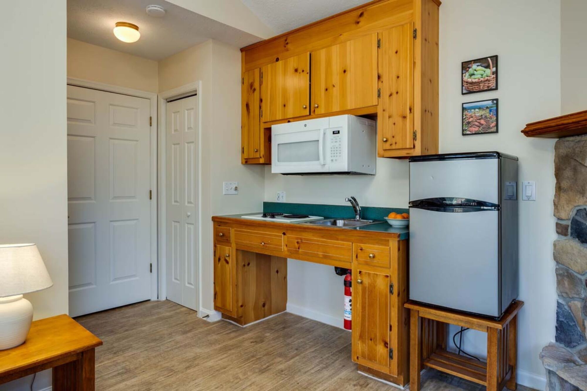 A compact kitchen with wooden cabinets, a microwave, a refrigerator, and a sink.