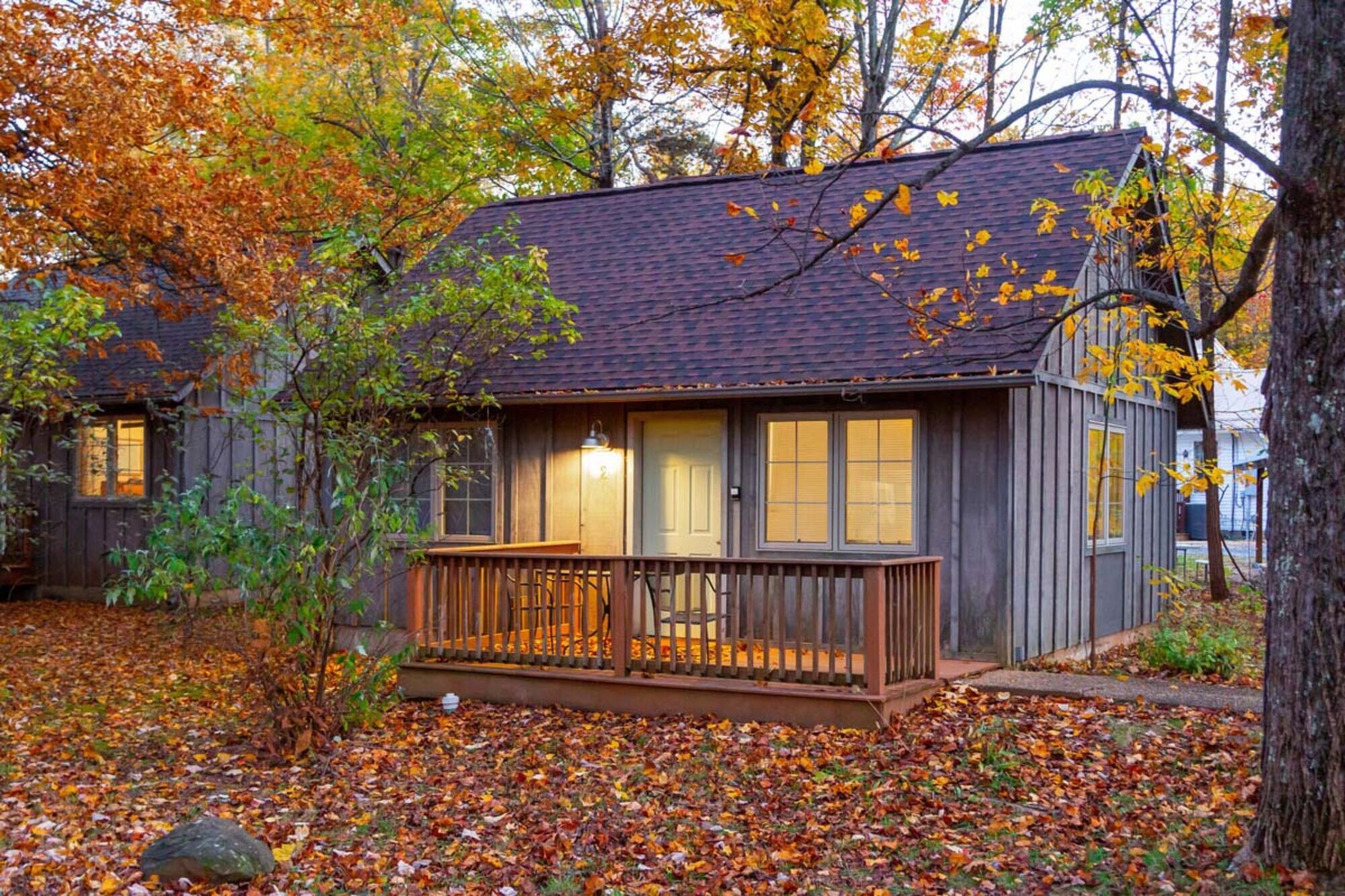 A cabin with a wooden deck and a porch, surrounded by autumn foliage.