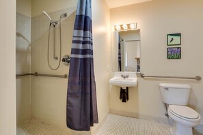 A bathroom with a shower, toilet, sink, and a mirror with lights. - White Rock Cabin--1BR, ADA, kitchenette, fireplace (Lyndhurst)