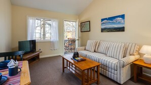 A living room with a sofa, a coffee table, a TV, and a dining area with chairs and a table. - White Rock Cabin--1BR, ADA, kitchenette, fireplace (Lyndhurst)