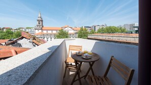 Une terrasse sur le toit, avec une table et des chaises, offrant une vue sur le paysage urbain, avec ses bâtiments historiques et le clocher d’une église.